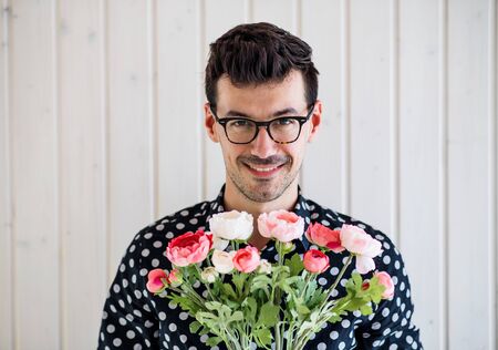 Young man with flowers standing against white wooden background wall.