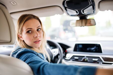 Young woman driver sitting in car, looking back.