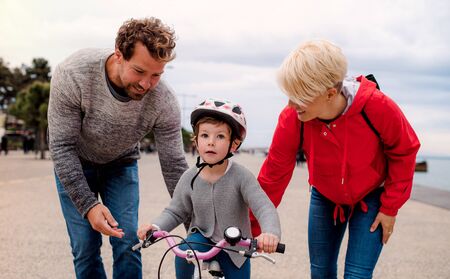 Young family and small daughter with bicycle outdoors on beach.の写真素材