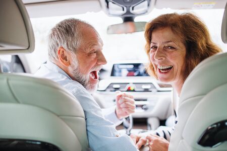 Rear view of happy senior couple sitting in car, looking back.の写真素材