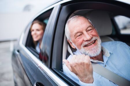 Senior man and young woman sitting in car, looking out of window.の写真素材