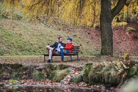 Senior father and his son sitting on bench by lake in nature, talking.の写真素材