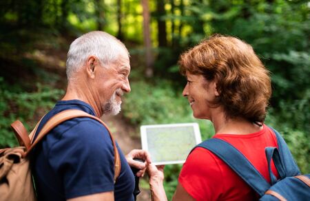Senior tourist couple on a walk in forest in nature, using map on tablet.の写真素材