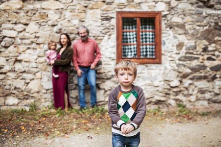 A small boy with his family standing in front of old stone house.の写真素材