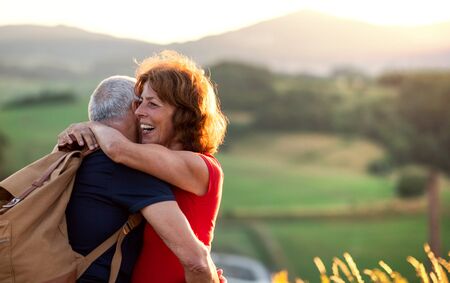 Senior tourist couple travellers with backpacks hiking in nature, hugging.の写真素材