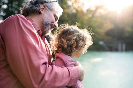 Mature father with toddler daughter standing by the lake on a walk.