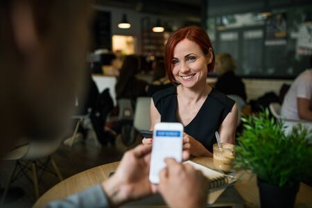 Midsection of businesspeople with smartphone in a cafe, checking finances.