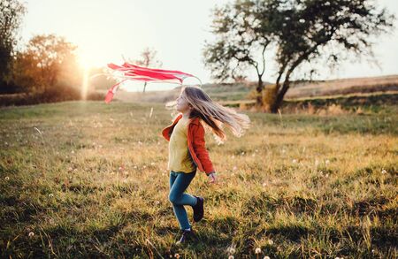 A small girl playing with a rainbow hand kite in autumn nature at sunset.の写真素材