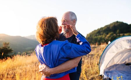 Senior tourist couple in love standing in nature at sunset, hugging.の写真素材