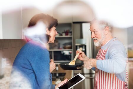A portrait of senior couple in love indoors at home, cooking.の写真素材
