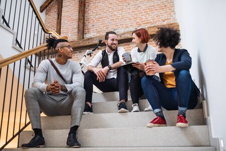 Group of young businesspeople sitting on stairs indoors, talking.の写真素材