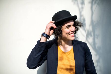 A happy young business woman standing outdoors, holding hat.
