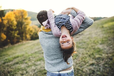 A rear view of young father having fun with a small daughter in autumn nature.の写真素材