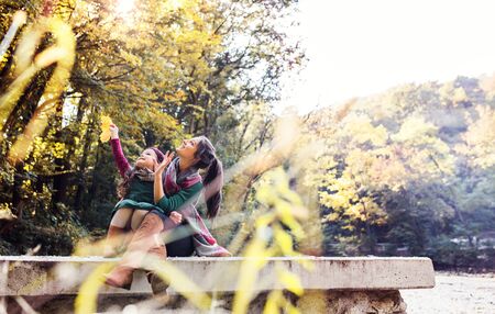 A mother with a toddler daughter sitting in forest in autumn nature.の写真素材
