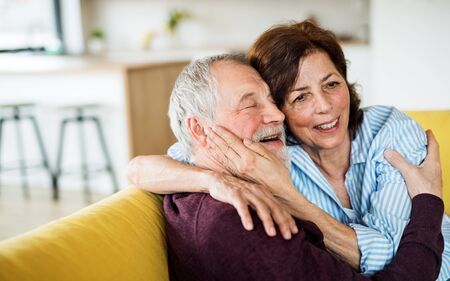 An affectionate senior couple in love sitting on sofa indoors at home.