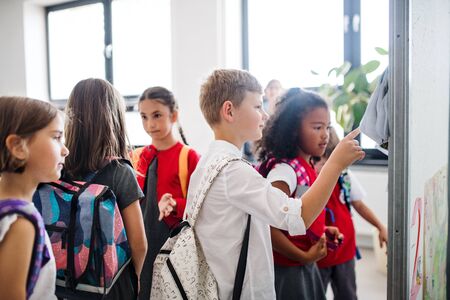 A group of cheerful small school kids with bags standing in corridor.の写真素材