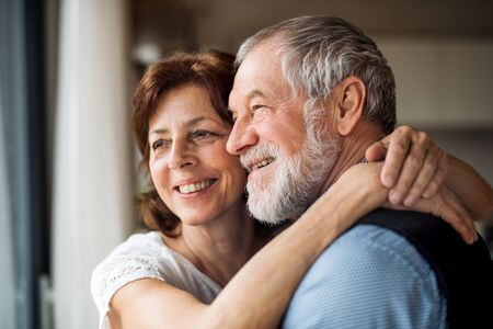 A senior couple indoors at home, looking out of window.の写真素材