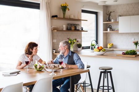Senior couple in love having lunch indoors at home, talking.の写真素材