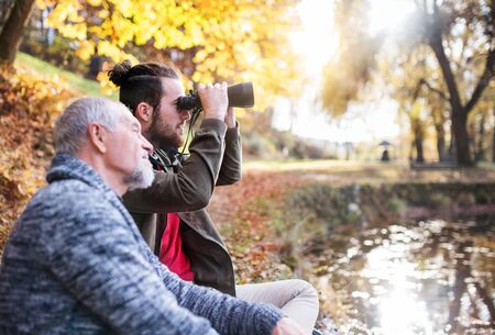 Senior father and his son with binoculars in nature, talking.の写真素材