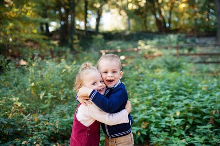 Twin toddler sibling boy and girl standing in autumn forest, hugging.の写真素材