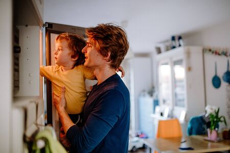 A young father with a toddler son in a kitchen at home.の写真素材