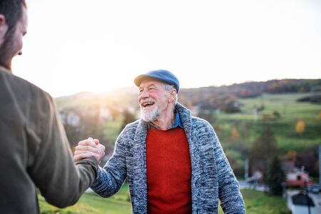 Laughing senior father and his son on walk in nature, shaking hands.の写真素材
