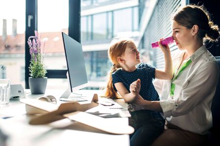 A businesswoman with small daughter sitting in an office, working.の写真素材