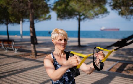 A young sportswoman doing exercise with TRX fitness straps outdoors.の写真素材