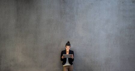 Young business woman with tablet standing against concrete wall in office.の写真素材