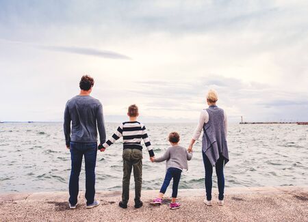 Rear view of young family with two small children standing outdoors on beach.の写真素材