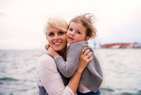 Young mother with small daughter standing outdoors on beach.