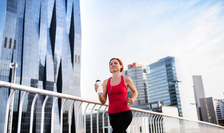 Young woman runner with earphones and water bottle jogging in city.の写真素材