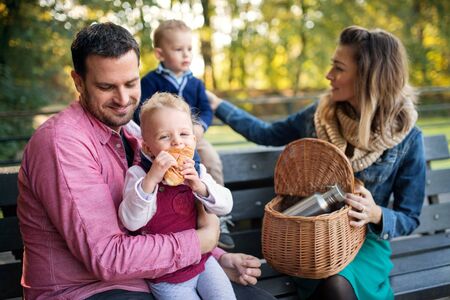 Beautiful young family with small twins sitting on bench in autumn park.の写真素材