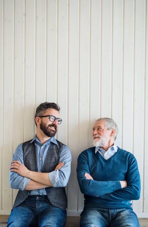 A portrait of adult hipster son and senior father sitting on floor indoors at home.の写真素材