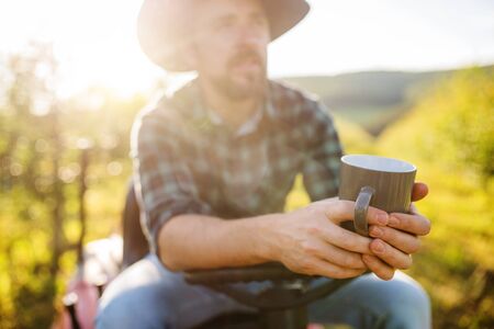 A mature farmer with cup of coffee outdoors in orchard, resting.の写真素材