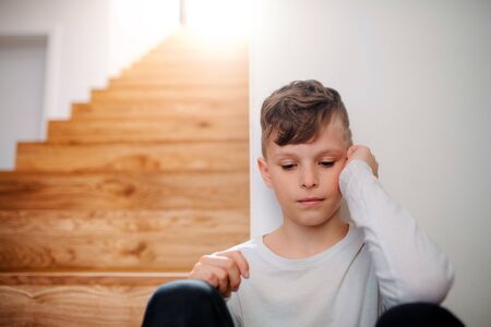 A small unhappy boy sitting on the floor by the stairs.