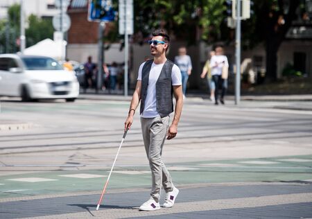 Young blind man with white cane walking across the street in city.の写真素材