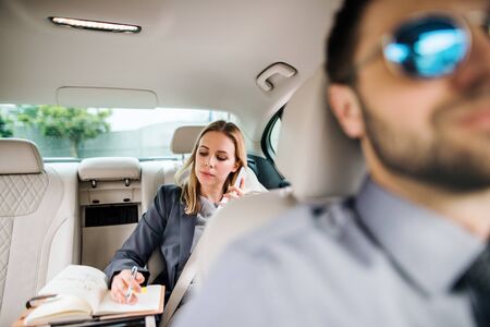 Business woman with smartphone sitting on back seat in taxi car, talking.の写真素材