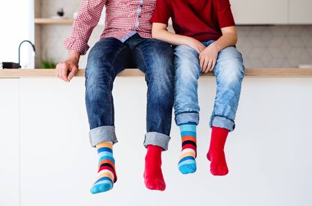 Midsection of father with son with funky socks sitting on kitchen counter indoors.の写真素材