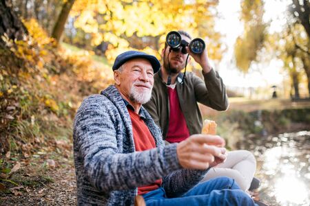 Senior father and his son with binoculars in nature, talking.の写真素材