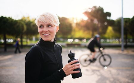 Portrait of young sportswoman standing outdoors in town, holding water bottle.の写真素材