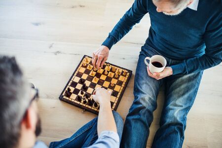 An adult hipster son and senior father sitting on floor indoors at home, playing chess.の写真素材