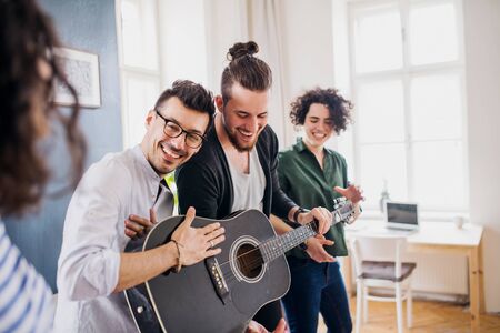 A group of young friends with guitar indoors at home, house sharing concept.の写真素材