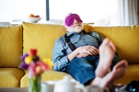 Senior man with eye mask lying on sofa indoors at home, relaxing.の写真素材