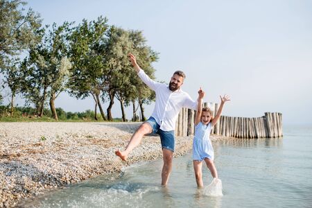 Mature father and small daughter on a holiday playing by the lake.の写真素材