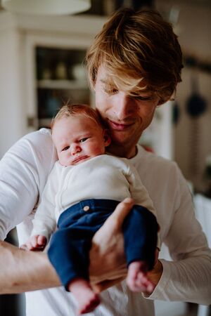 A front view of young father holding a newborn baby at home.