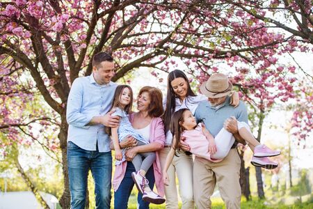 Three generation family standing outside in spring nature, looking at camera.