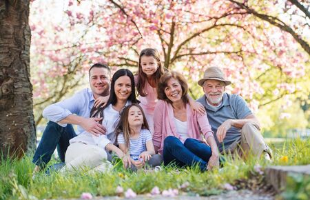 Three generation family sitting outside in spring nature, looking at camera.の写真素材