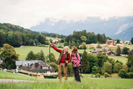 Senior pensioner couple with nordic walking poles hiking in nature, talking.の写真素材