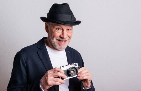 Portrait of a senior man with hat and camera in a studio.の写真素材